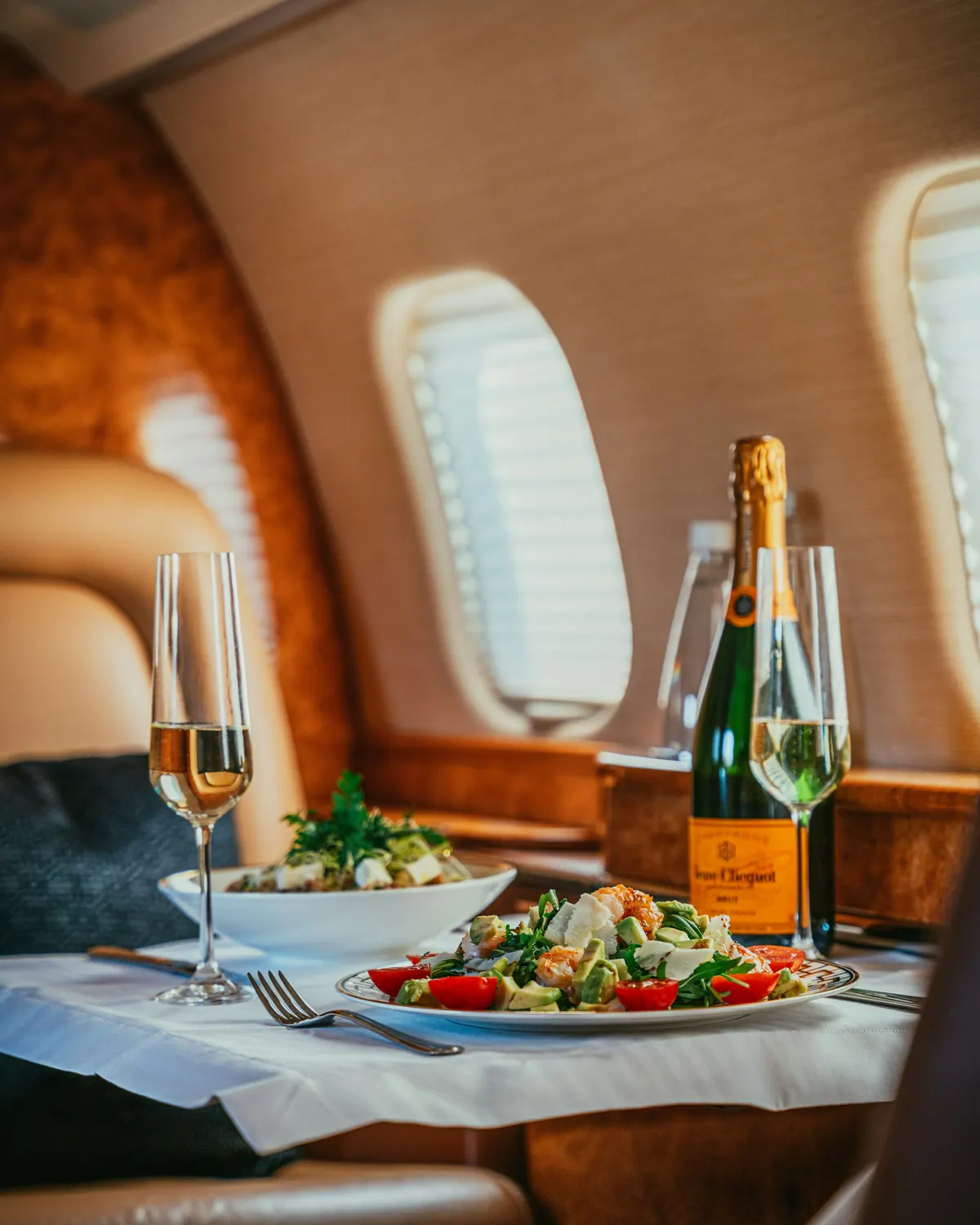 A table set with salad and champagne beside a cabin window on a private jet